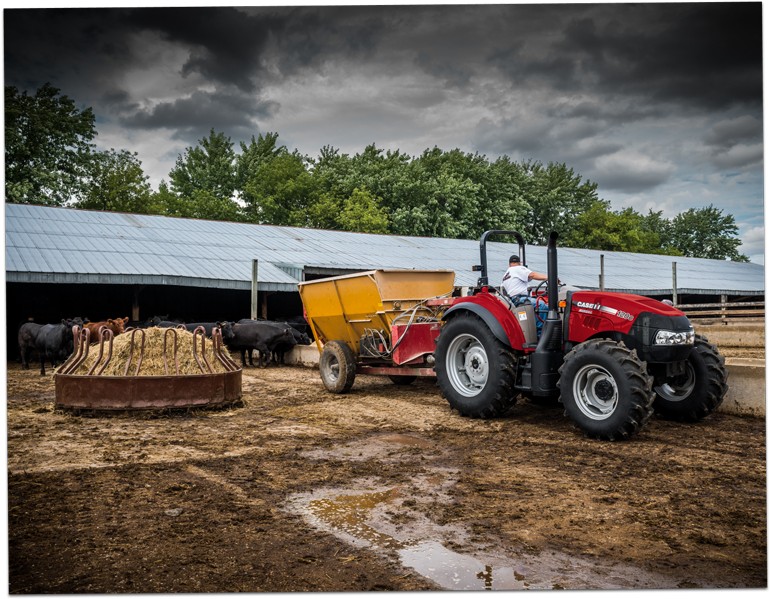 Modern Farmall tractor pulling a trailer on a farm