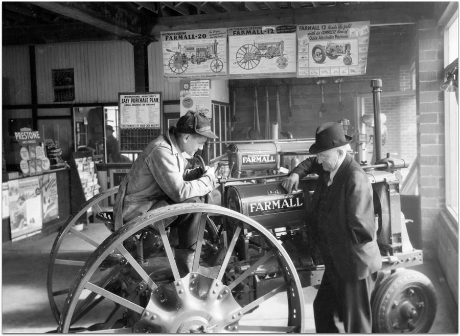 Black and white image of two men looking at the 1931 Farmall F series tractor in dealership