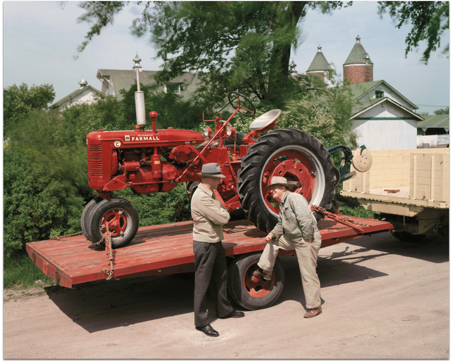 Farmall tractor on trailer with Two men standing in front of trailer