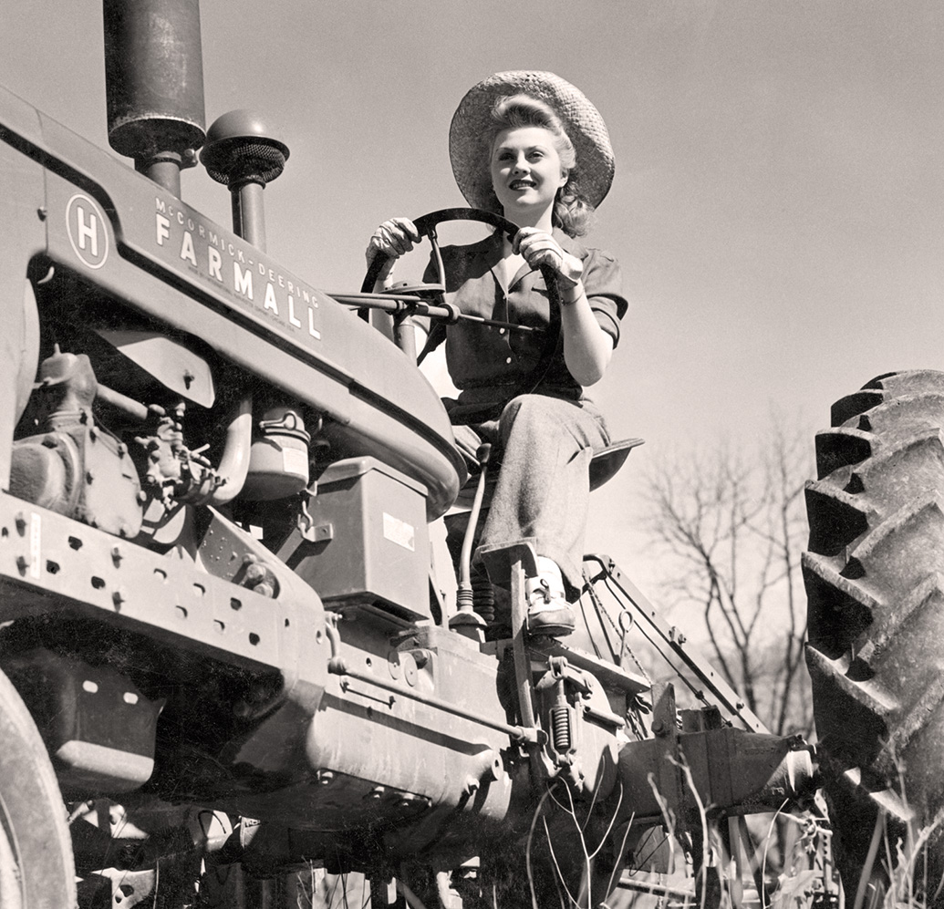 Black and white image of a woman driving a Farmall tractor